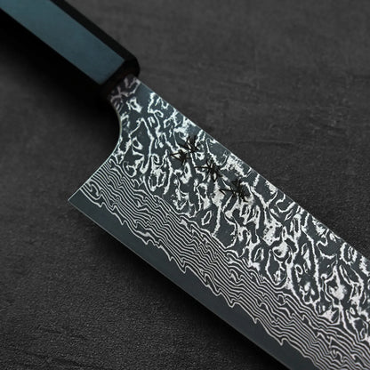 Three ants walk on a kiritsuke gyuto knife with a damascus blade and a black handle.