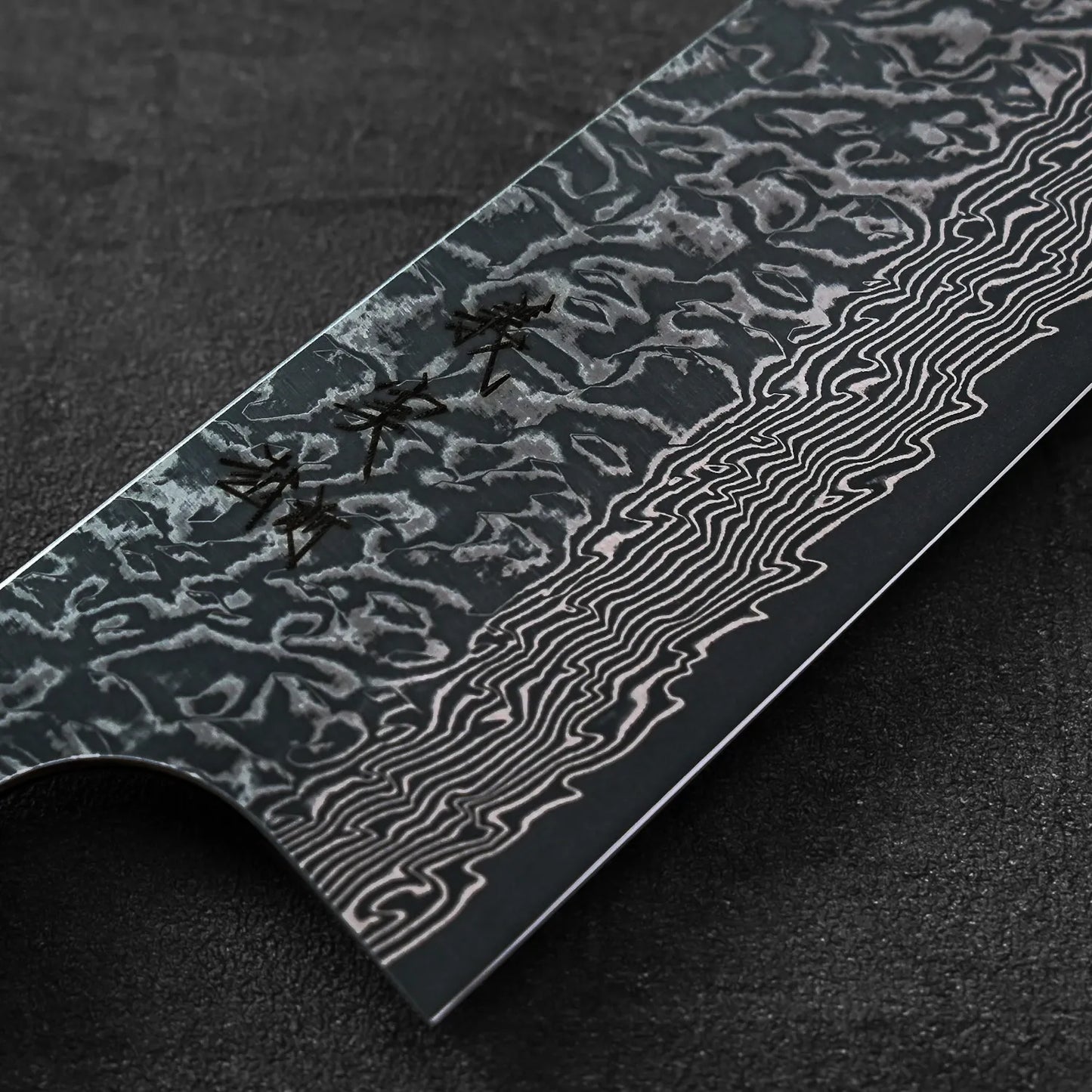 Kiritsuke gyuto blade in close-up with wavy patterns and textured damascus steel visible on the surface.