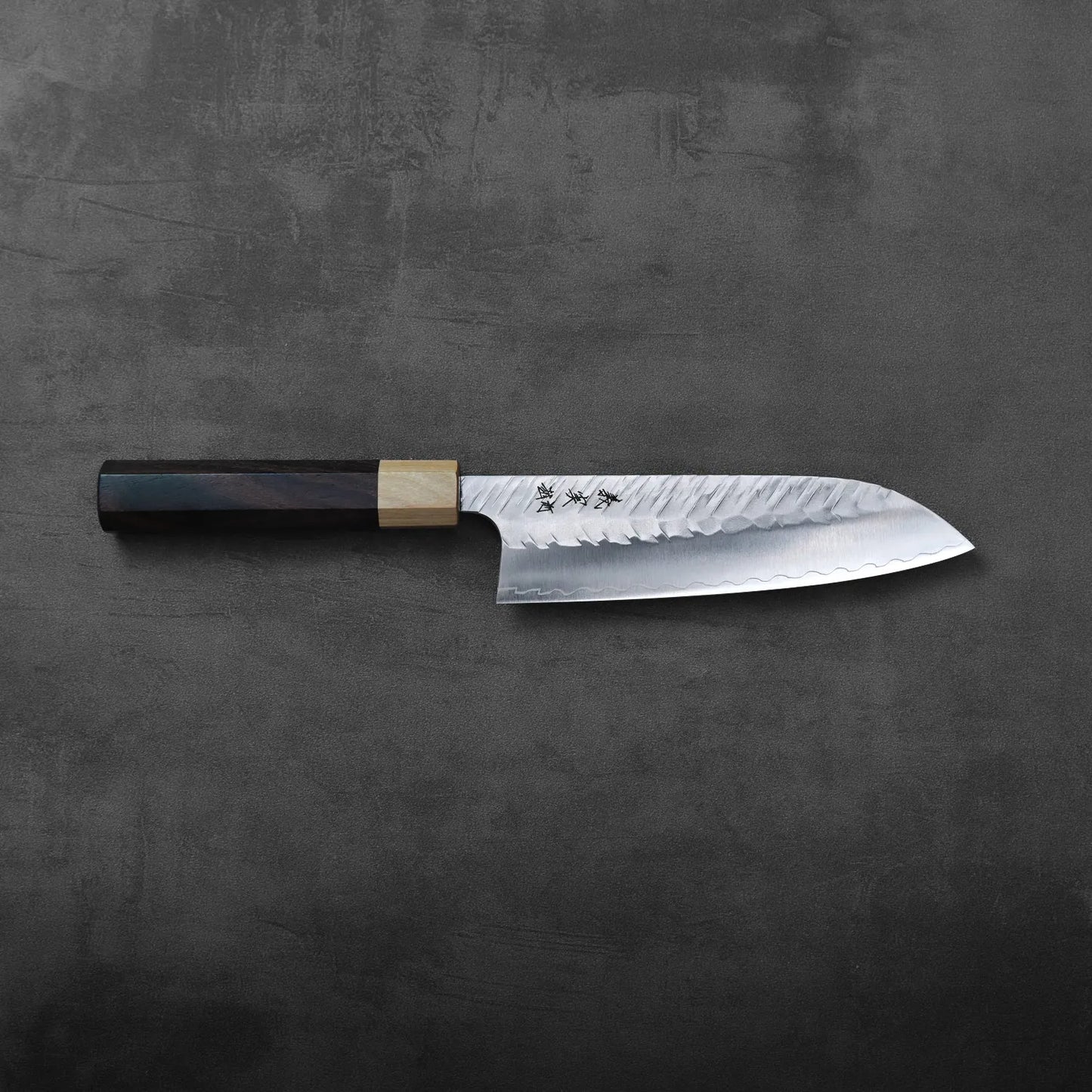 Santoku with a patterned blade and dark wood handle, highlighting the textured metal and grain detail.