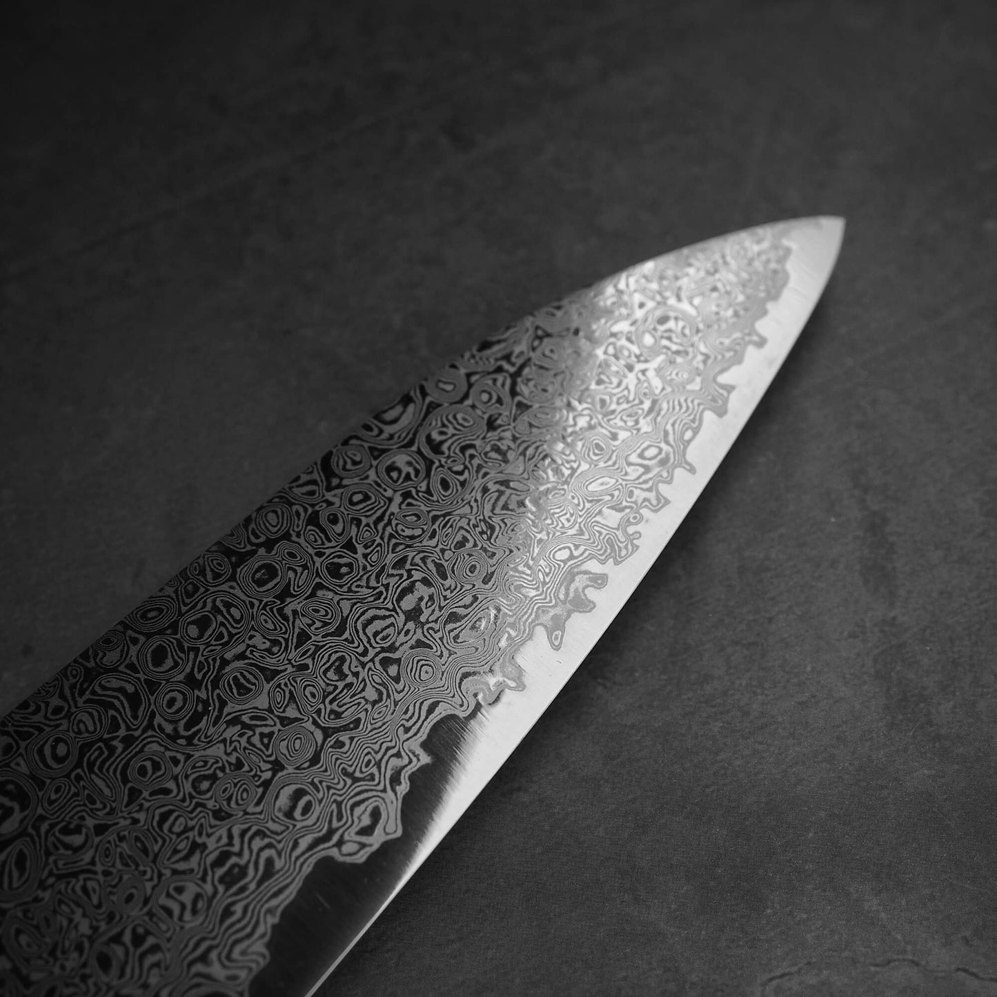 Close up view of the blade of Hatsukokoro ginsan damascus gyuto 210mm. Image focuses on the tip area of the front side of theblade