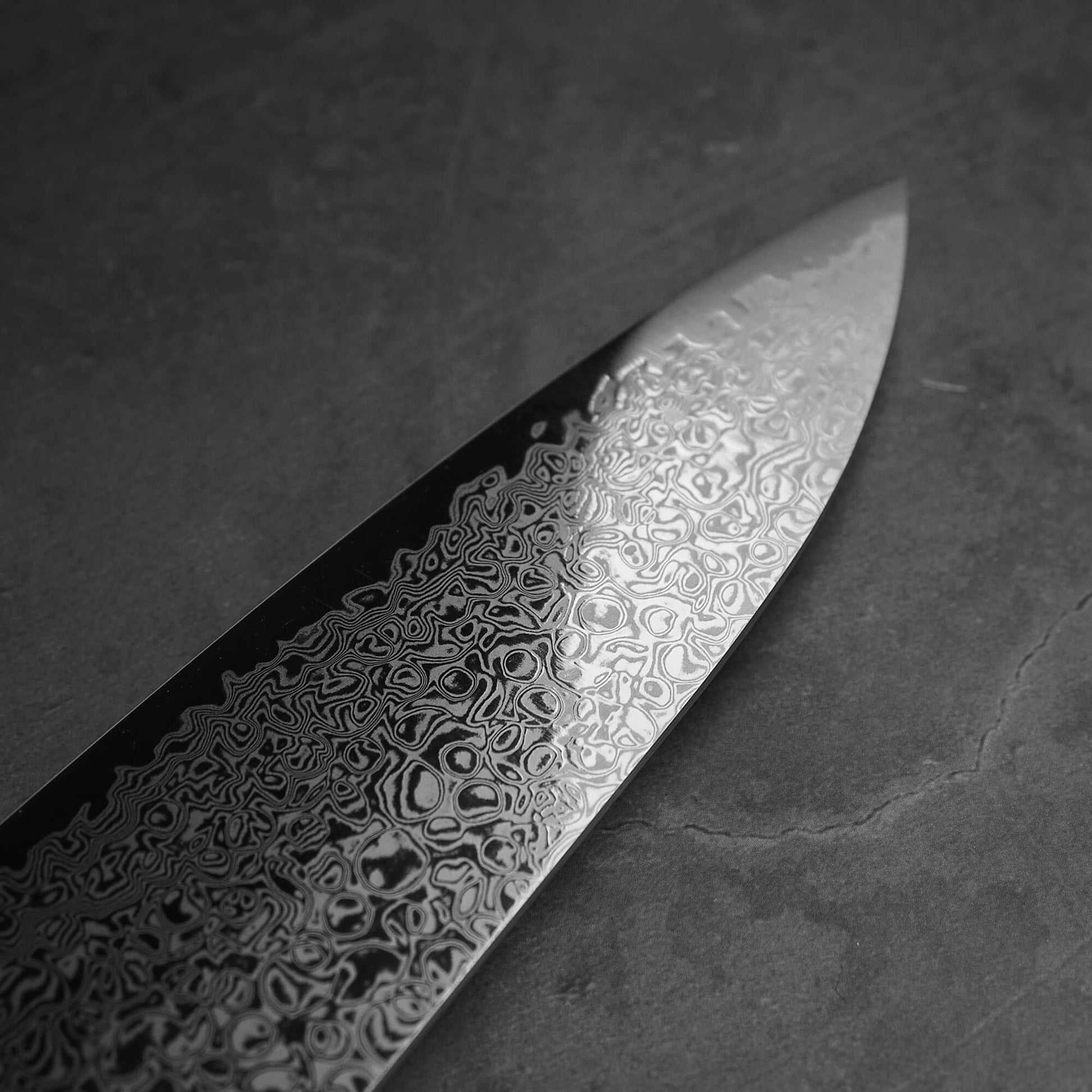 Close up view of Hatsukokoro ginsan damascus gyuto 240mm. Image focuses on the tip area of left side of the blade.
