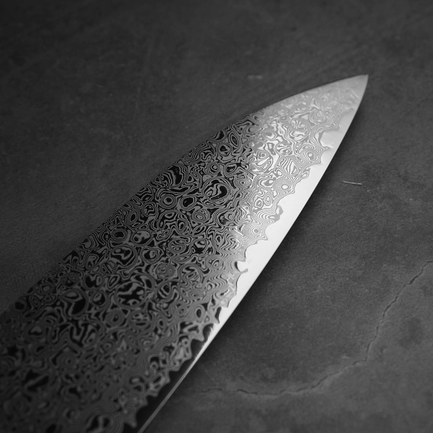 Close up view of Hatsukokoro ginsan damascus gyuto 240mm. Image focuses on the tip area on the right side of the blade.