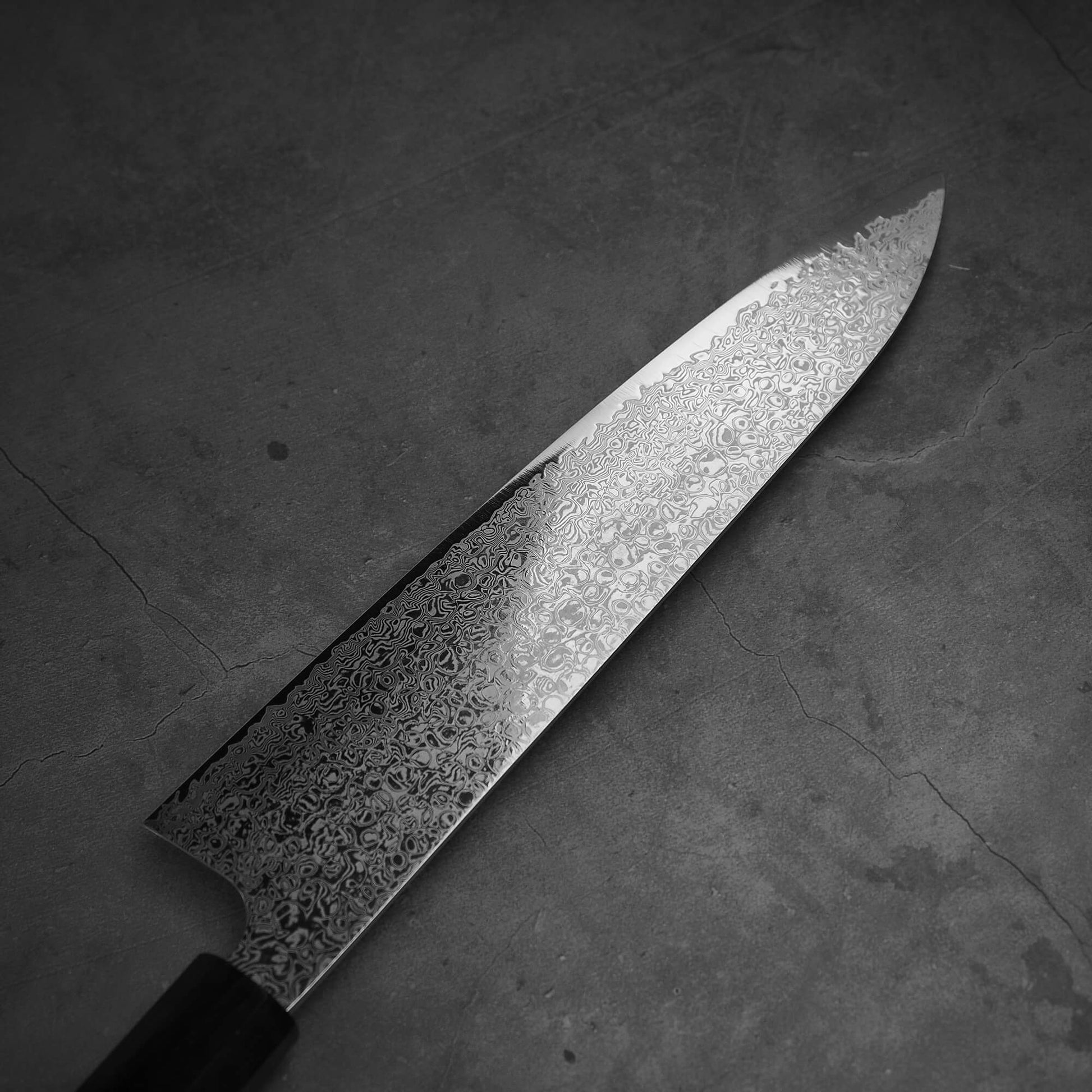 Top view of Hatsukokoro ginsan damascus gyuto 240mm. Image focuses on the left side of the blade.
