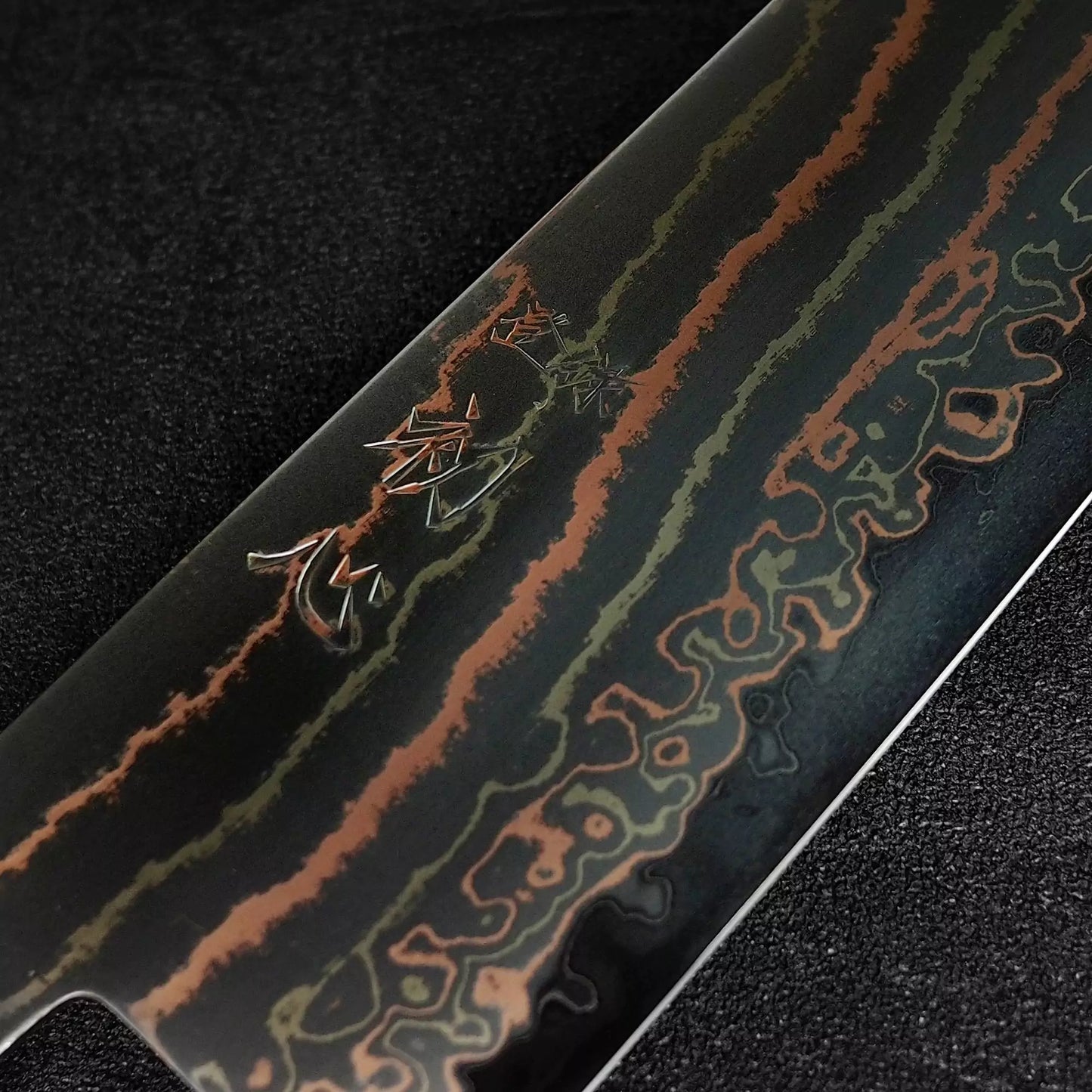 Close up view of the kanji of Hatsukokoro Habayusa aogami#2 rainbow damascus santoku knife