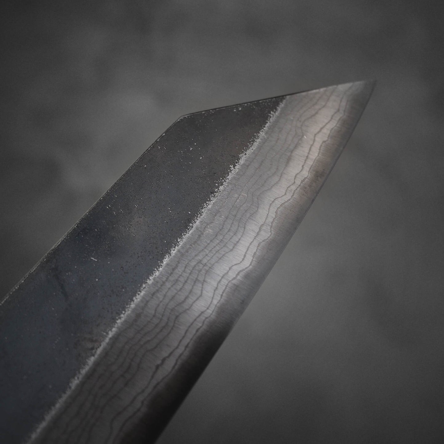 Close up view of Hatsukokoro Kumokage kurouchi damascus aogami#2 bunka knife. Image shows the tip area of the right side of the blade.