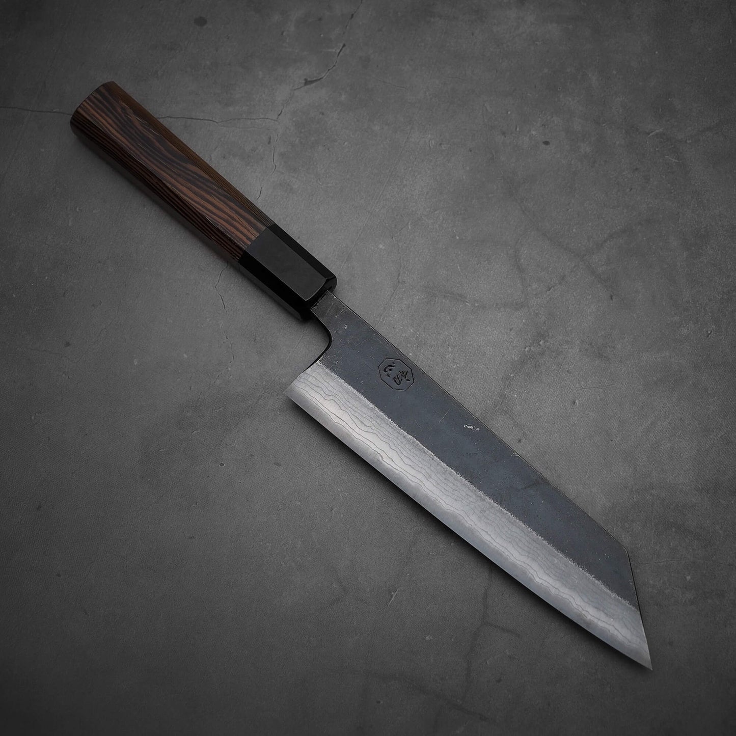 Top view of Hatsukokoro Kumokage kurouchi damascus aogami#2 bunka knife where tip is facing lower right