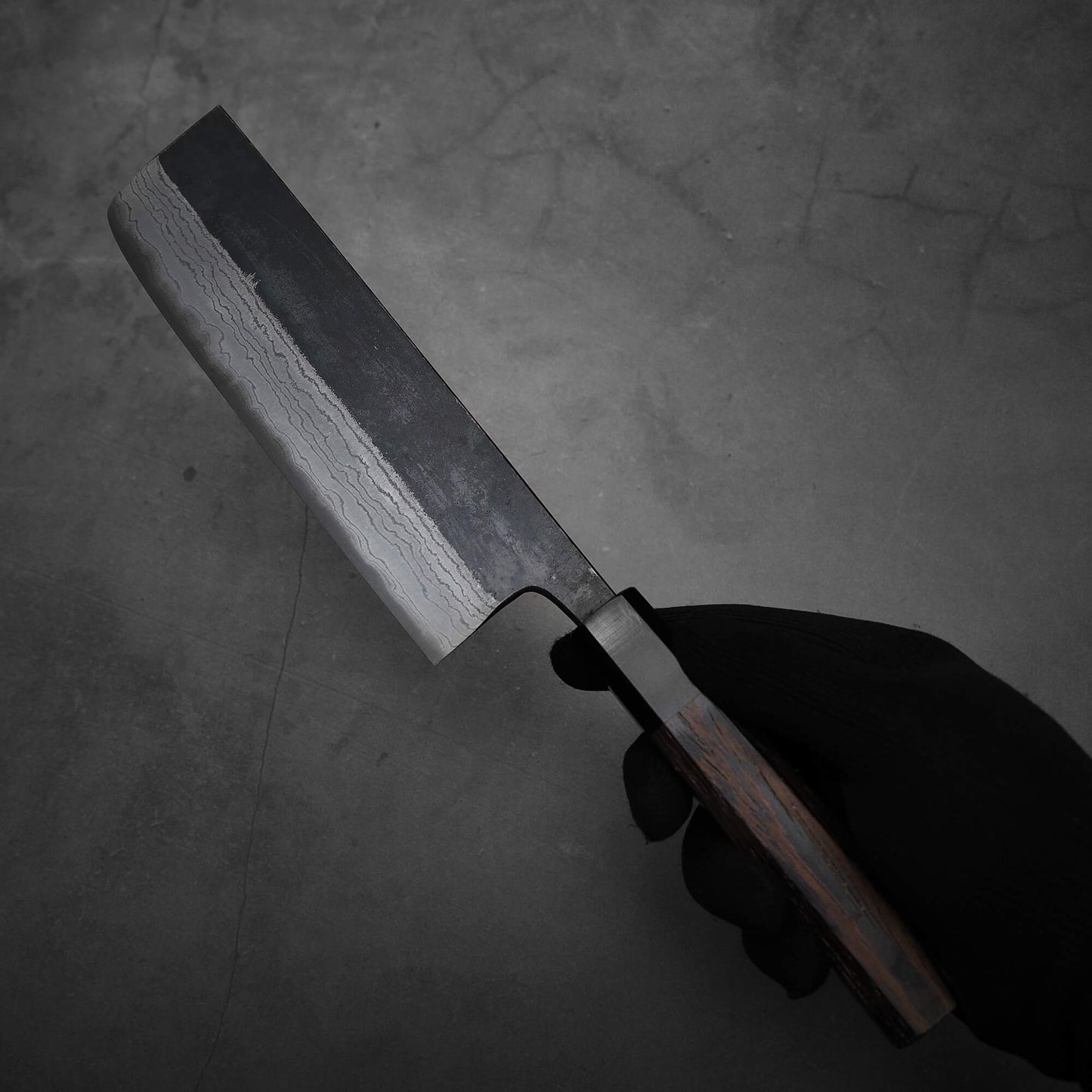 Hand holding Hatsukokoro Kumokage kurouchi damascus aogami#2 nakiri knife where the left side of the blade is shown