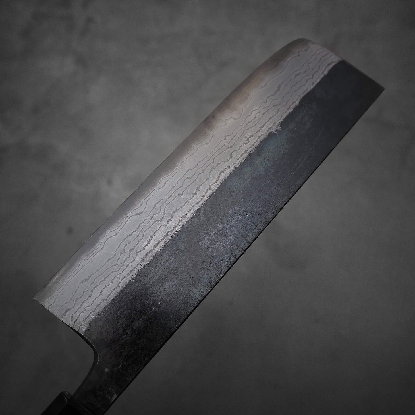 Top view of Hatsukokoro Kumokage kurouchi damascus aogami#2 nakiri knife. Image shows left side of the blade