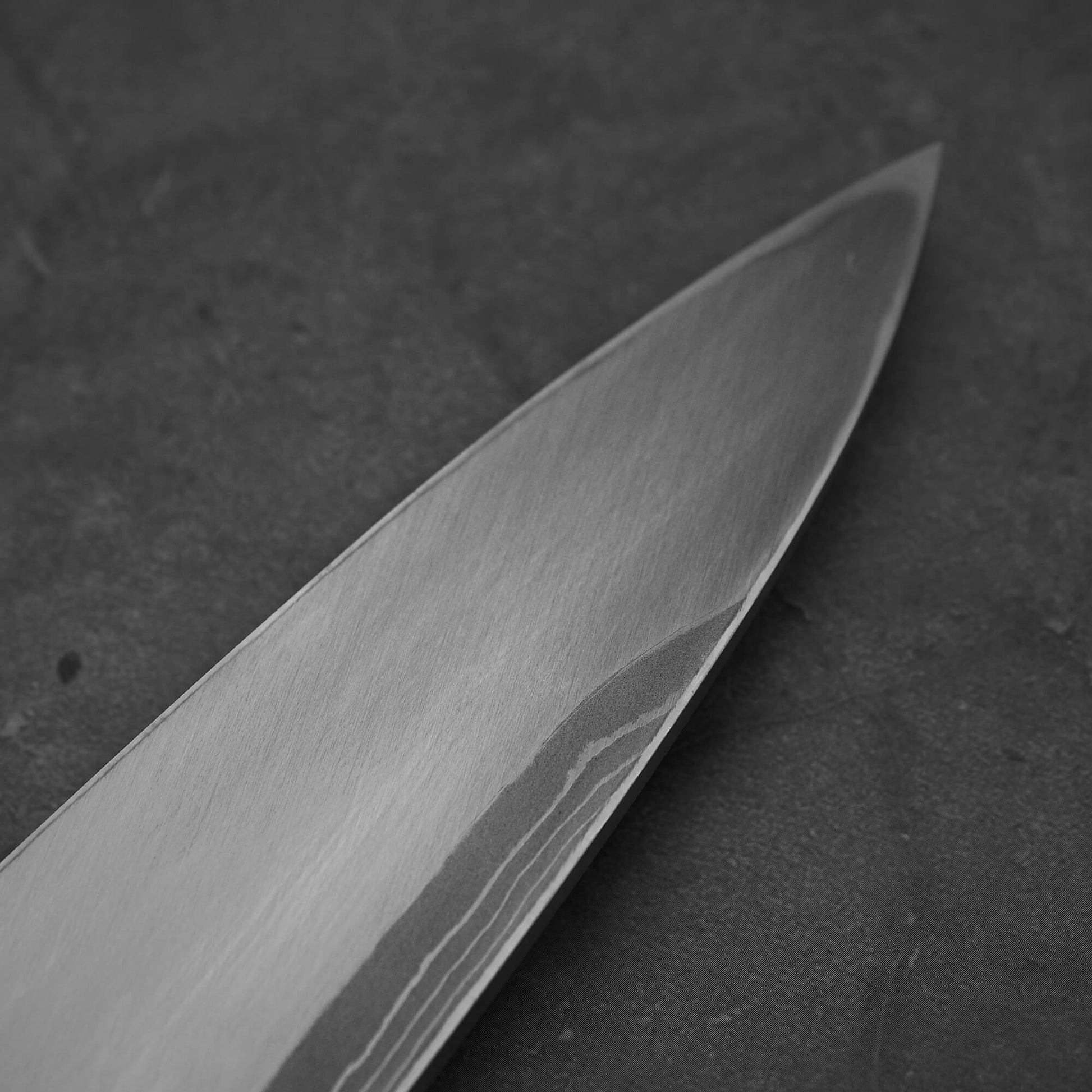 Close up view of Hideo Kitaoka damascus aogami#2 mioroshi deba 210mm. Image focuses on the tip area of the back side of the knife