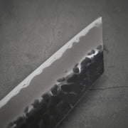 Close up view of Ittosai Kotetsu tsuchime kurouchi aogami super kiritsuke gyuto. Image focuses on the tip area of the back side