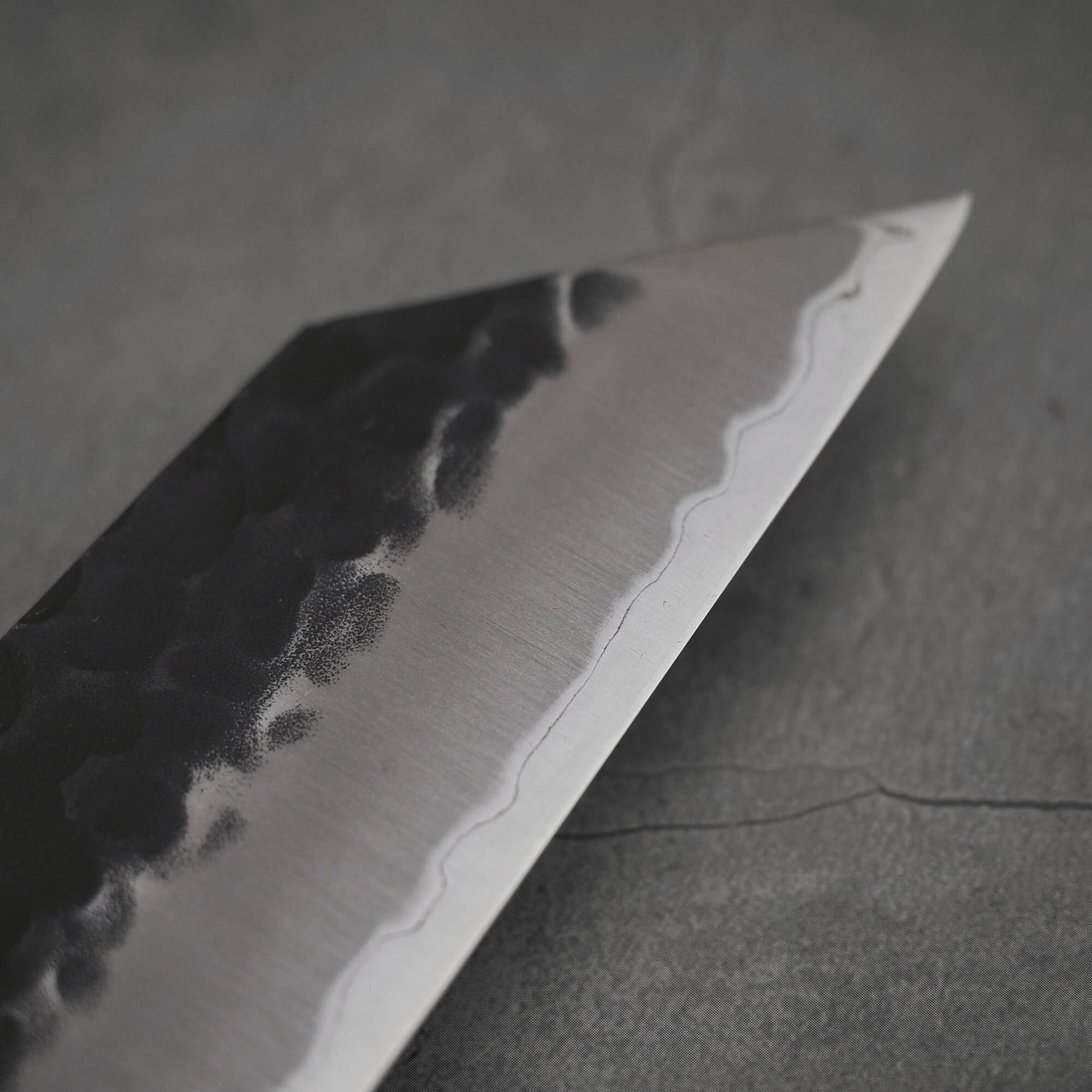 Close up view of Ittosai Kotetsu tsuchime kurouchi aogami super kiritsuke gyuto. Image focuses on the tip area of the right side of the blade