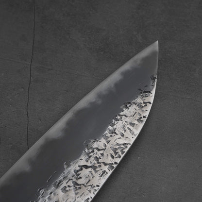 Close up view of a 220mm Kisuke Manaka tsuchime honwarikomi shirogami#2 gyuto knife. Image shows the tip area of the left side of the blade.