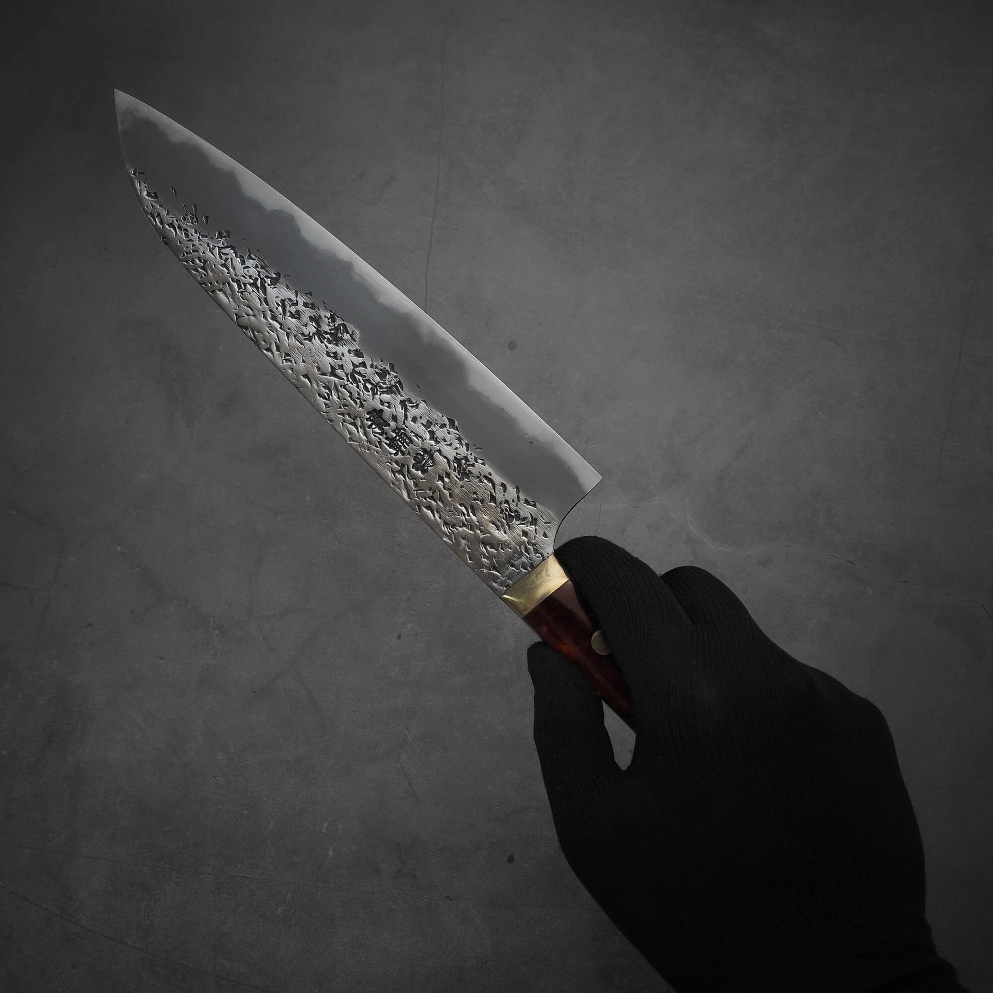 Hand holding a 220mm Kisuke Manaka tsuchime honwarikomi shirogami#2 gyuto knife. The pointed tip facing towards the upper left