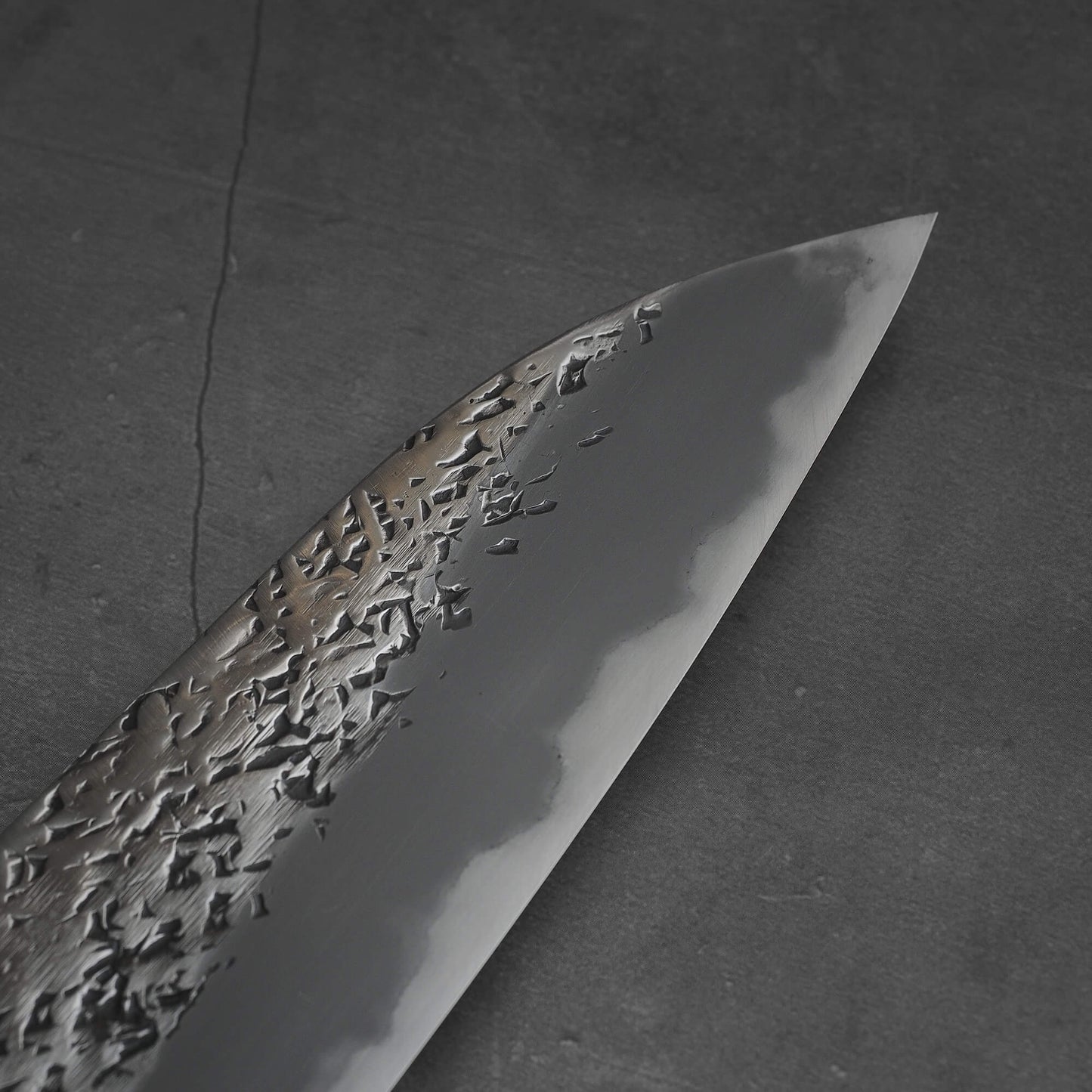 Close up view of 220mm Kisuke Manaka tsuchime honwarikomi shirogami#2 gyuto knife. Image shows the tip area on the right side of the knife