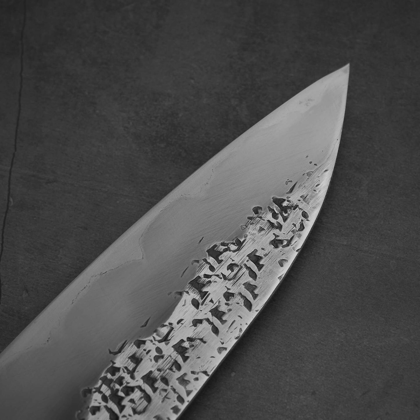 Close up view of 240mm Kisuke Manaka tsuchime honwarikomi shirogami#2 gyuto knife. Image focuses on the tip area on the left side of the knife