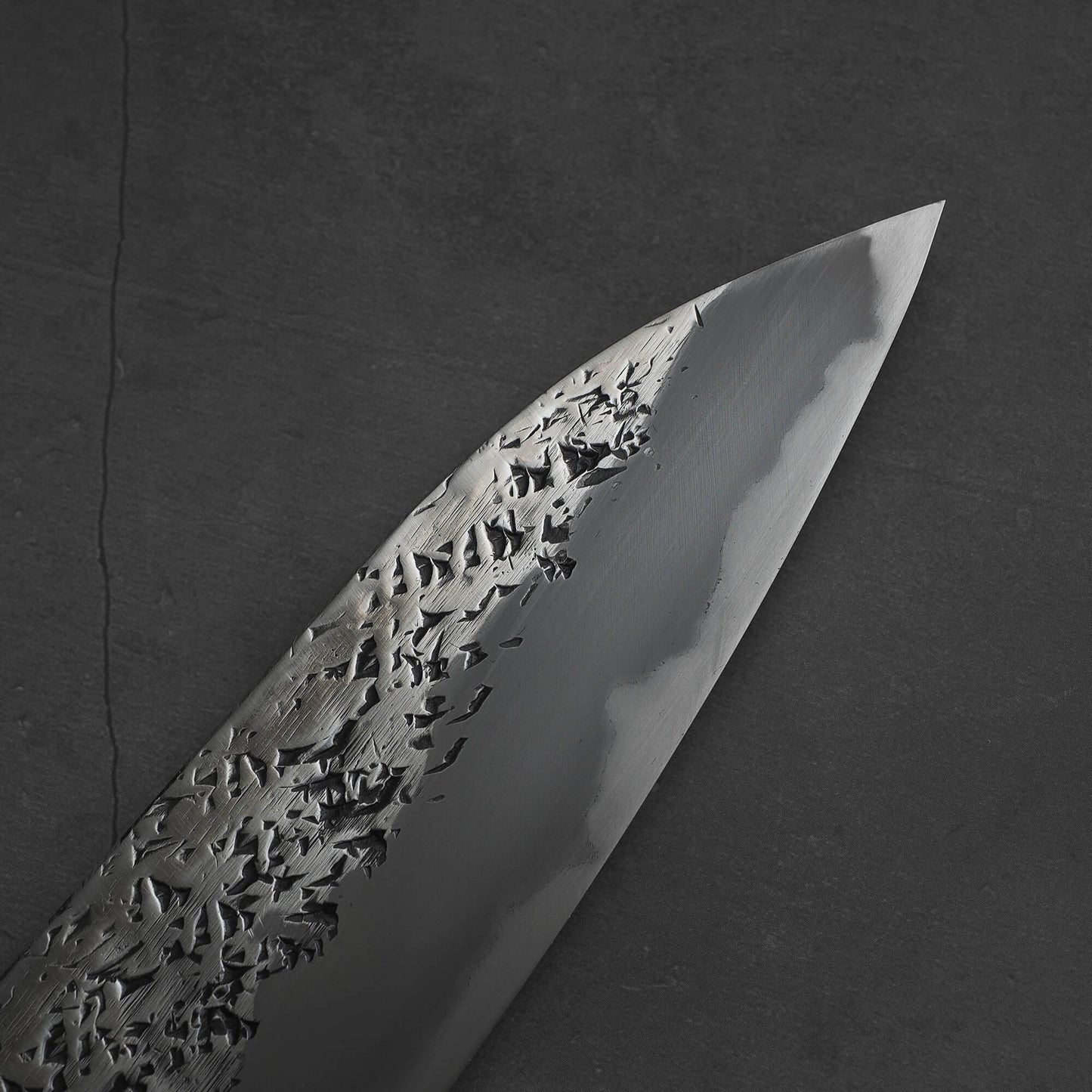 Close up view of 240mm Kisuke Manaka tsuchime honwarikomi shirogami#2 gyuto knife. Image shows the tip area of the right side of the blade