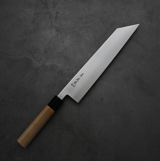 The Masamoto MV kiritsuke gyuto 240mm, featuring a straight wooden handle and angular MV stainless steel blade engraved with Japanese characters, rests on a dark gray textured surface.