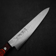 A Shigeki Tanaka VG10 damascus 150mm petty knife with a wavy pattern and engraved characters is placed on a dark textured surface.