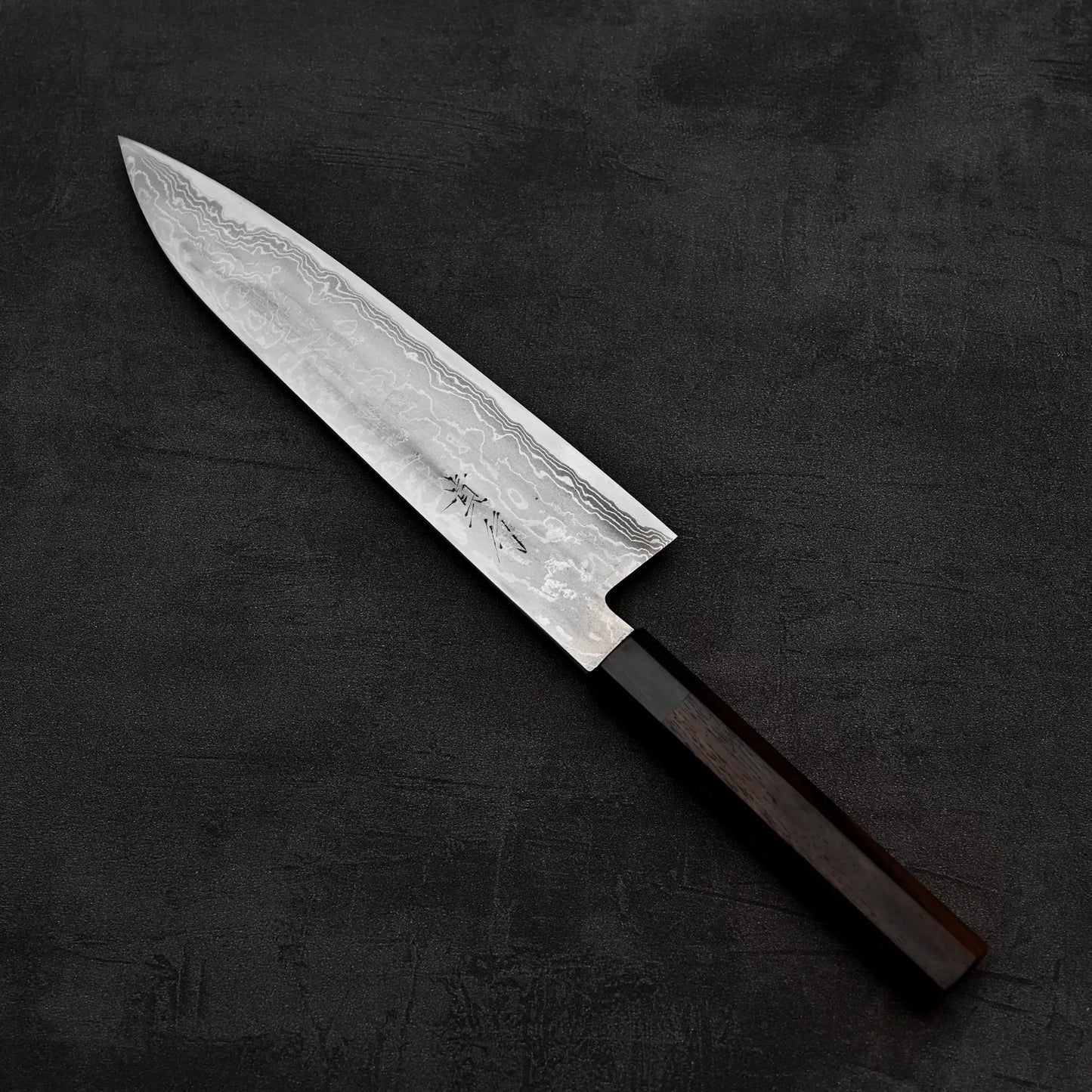Top down view of Takayuki Iwai aogami#2 damascus 240mm gyuto knife where pointed tip is facing towards the upper left