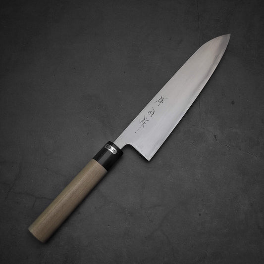The Toyama aogami#2 gyuto 210mm by Toyama, featuring a wooden handle and a broad, sharp blade of aogami #2 steel engraved with Japanese characters, rests on a dark, textured surface.