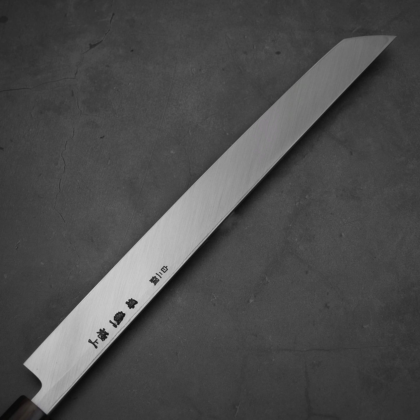 Close up view of Yoshikazu Tanaka sakimaru takohiki knife with a hand-forged blade made of shirogami#2 steel. Image shows the back side of the knife