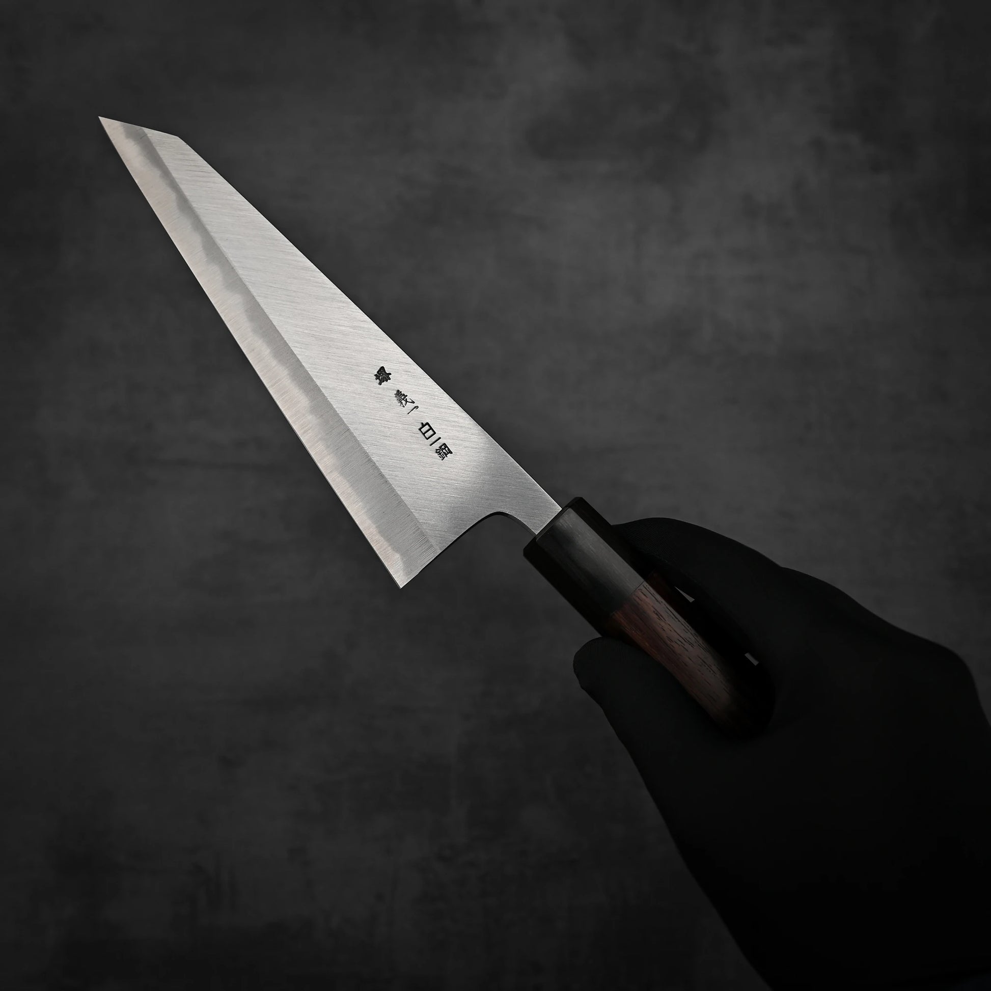 A hand holding a Yoshikazu Tanaka shirogami#1 double bevel honesuki knife showing the back side of the blade