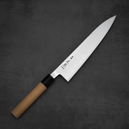 The Masamoto KS gyuto 210mm by Masamoto features a wooden handle and a sharp, pointed Shirogami#2 steel blade with kanji characters, shown on a dark, textured surface.