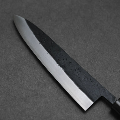 A close-up of the Ohishi kurouchi SLD gyuto 210mm Japanese chef knife by Ohishi, featuring a polished blade with a dark, textured section near the spine, displayed on a dark gray surface.