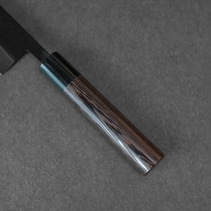 A close-up of the Ohishi kurouchi SLD gyuto 210mm chef knife by Ohishi, featuring a dark, polished wooden handle with visible grain, resting on a textured dark gray surface.