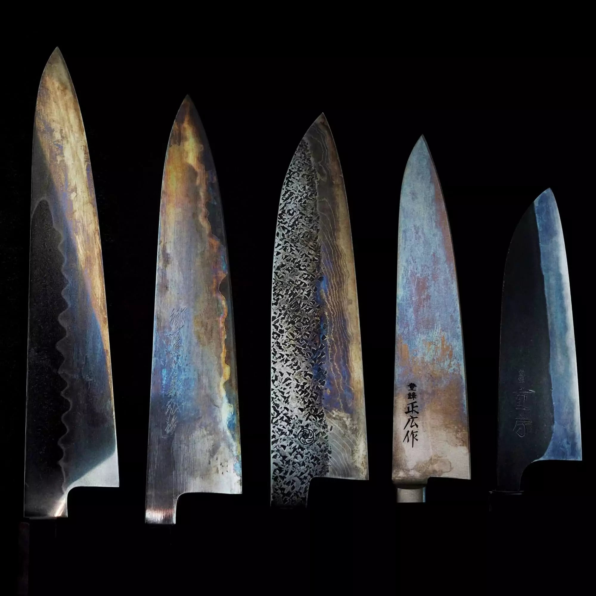 Five Japanese knives lined up against a dark background, each showcasing distinct patina.
