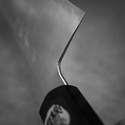 Close-up black and white photo of the Shigeki Tanaka ginsan gyuto 240mm blade, angled diagonally. The handle and spine of this Japanese kitchen knife are partially visible, set against a smooth, blurred background.