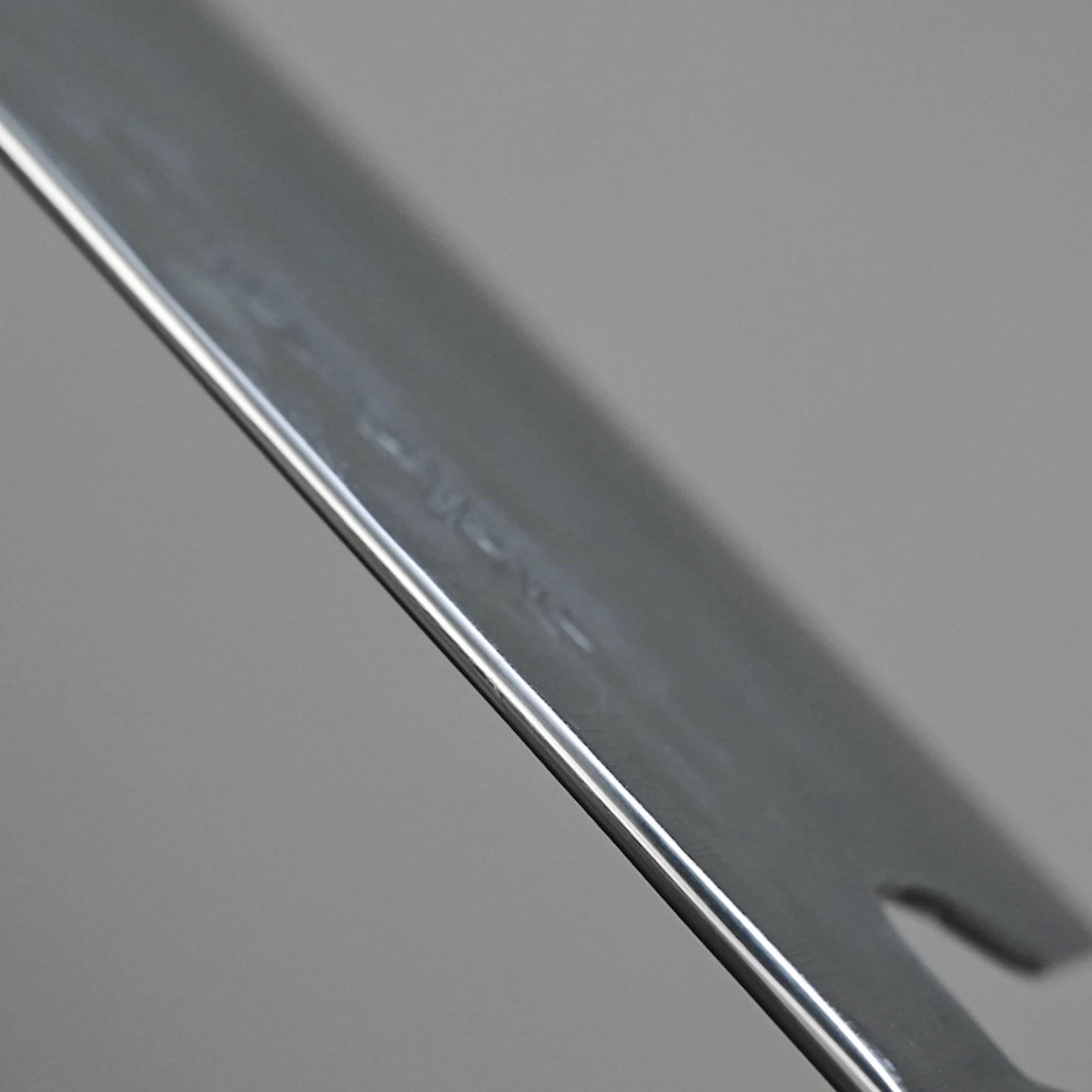 Close-up of the Teruyasu Fujiwara Maboroshi shirogami#1 nakiri 165mm, showcasing its polished spine and choil, smooth reflective edge, and a small notch, set against a plain gray background.