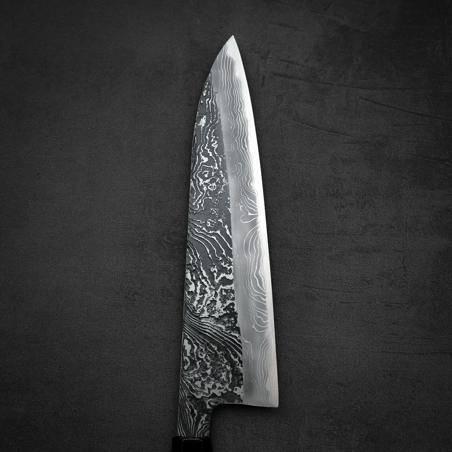 Close up view of the front blade of Yoshihide Masuda shirogami#2 kurouchi damascus tall gyuto knife in vertical position