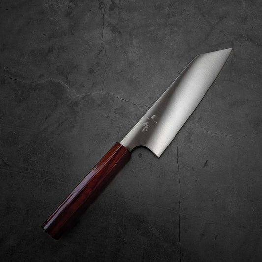 A chef’s knife with a polished wooden handle and a sharp, stainless steel blade rests on a dark, textured stone surface.