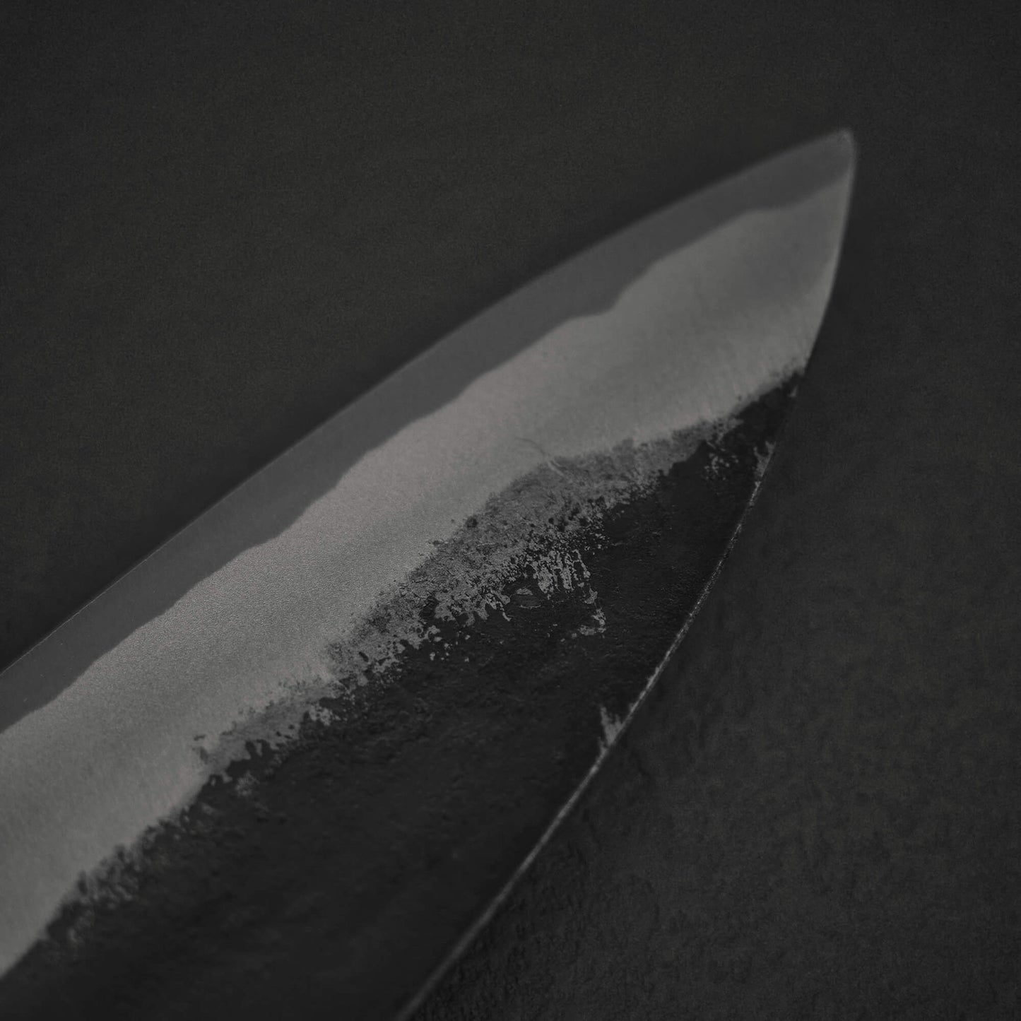 Close up view of Murata Buho kurouchi aogami#1 funayuki knife. Image focuses on the tip area of the left side of the blade.