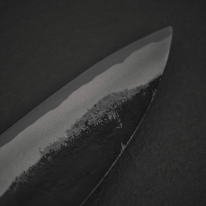 Close up view of Murata Buho kurouchi aogami#1 funayuki knife. Image focuses on the tip area of the left side of the blade.